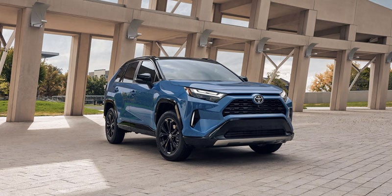 A blue SUV with a black roof and black wheels is parked on a paved surface next to a modern building with large pillars.