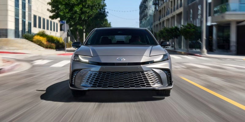 Front view of a gray 2023 Toyota Crown driving towards the camera on a city street.