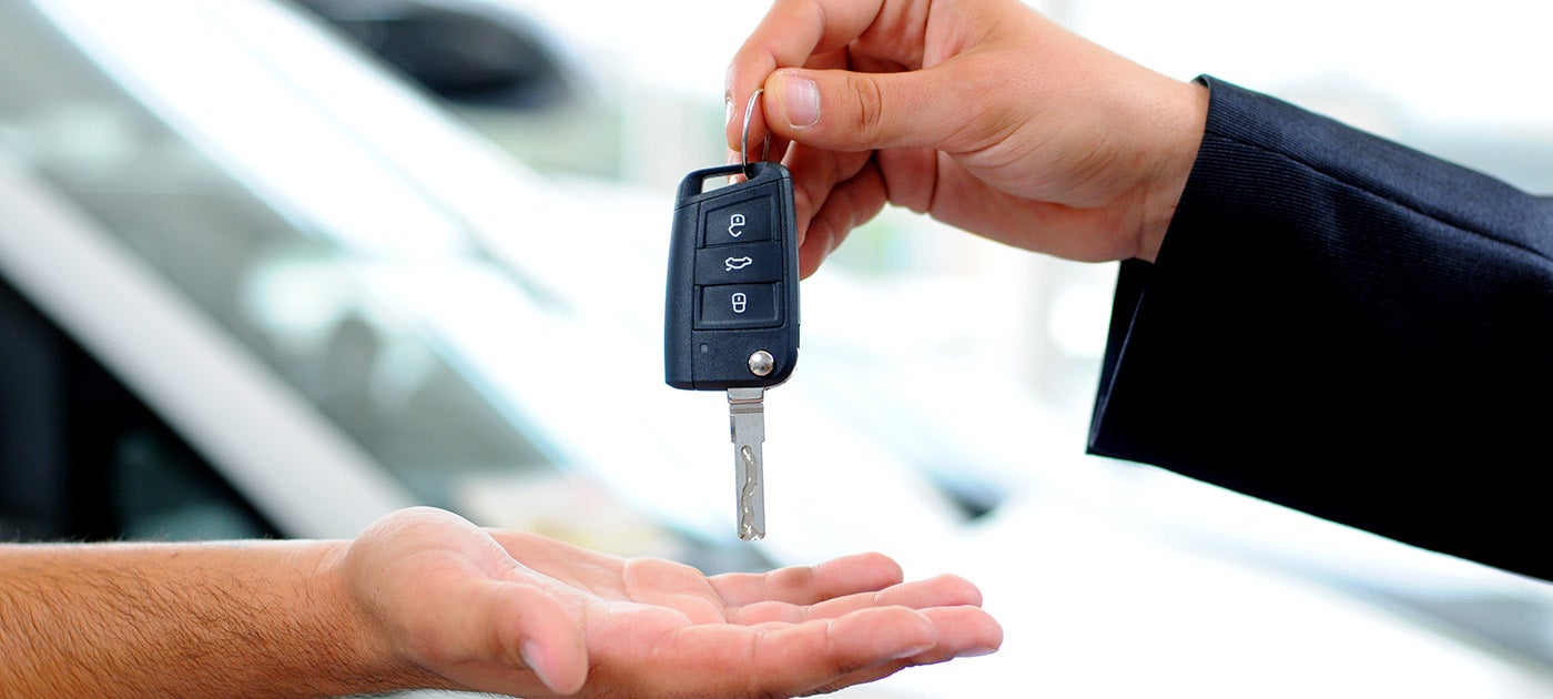 A person in a suit hands a car key to another person's open palm.