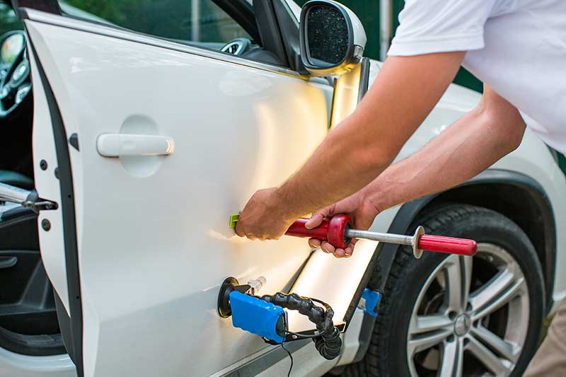 Close-up of a person using specialized tools to repair a dent on the white door of a car.