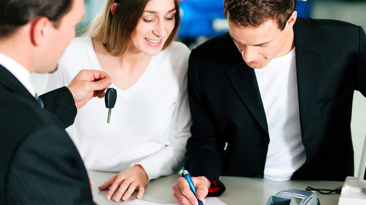 A couple signing paperwork at a dealership while receiving their new keys.